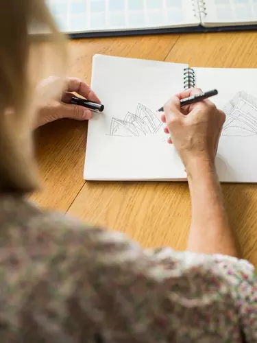 A woman drawing sketches of the Sydney Opera House in a notebook.