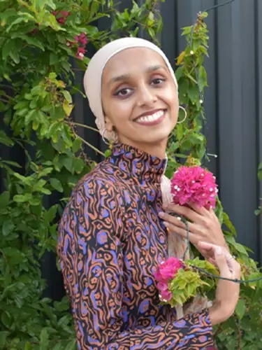 A woman holding a flower, wearing a head scarf.