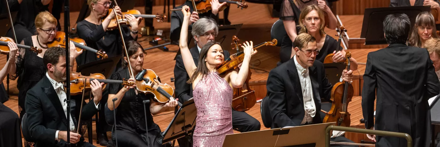 Violinist Arabella Steinbacher in a pink sequin dress flourishes the violin in front of the Sydney Symphony Orchestra violin section