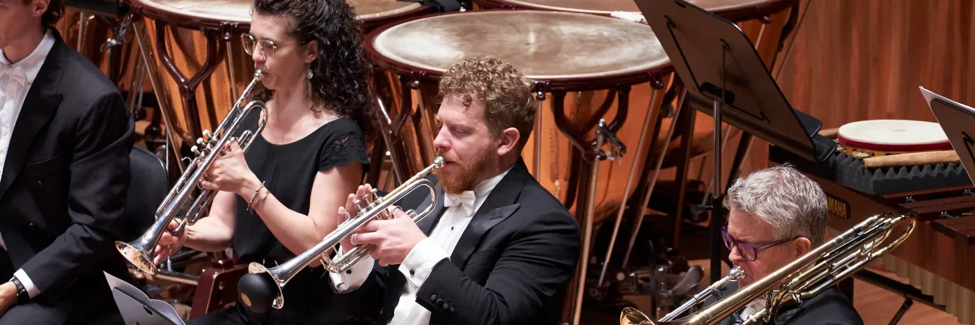 Three trumpet players of the Sydney Symphony Orchestra play the trumpet in front of the Timpani and percussion section