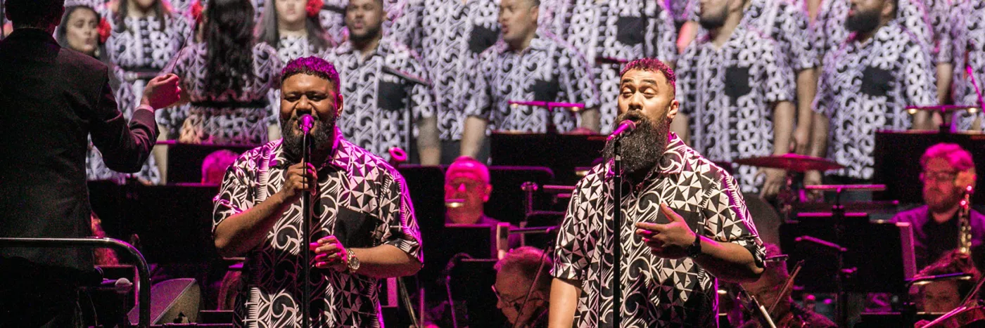 The Signature Choir in matching black and white designed shirts sing in front of an orchestra