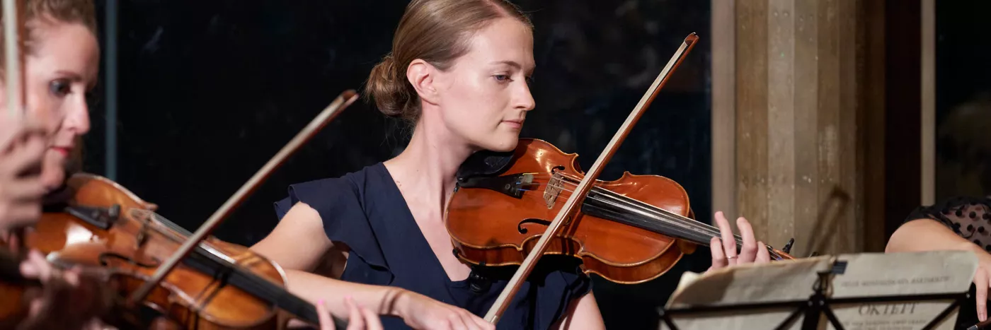 Two violin players stand in front of a marble wall
