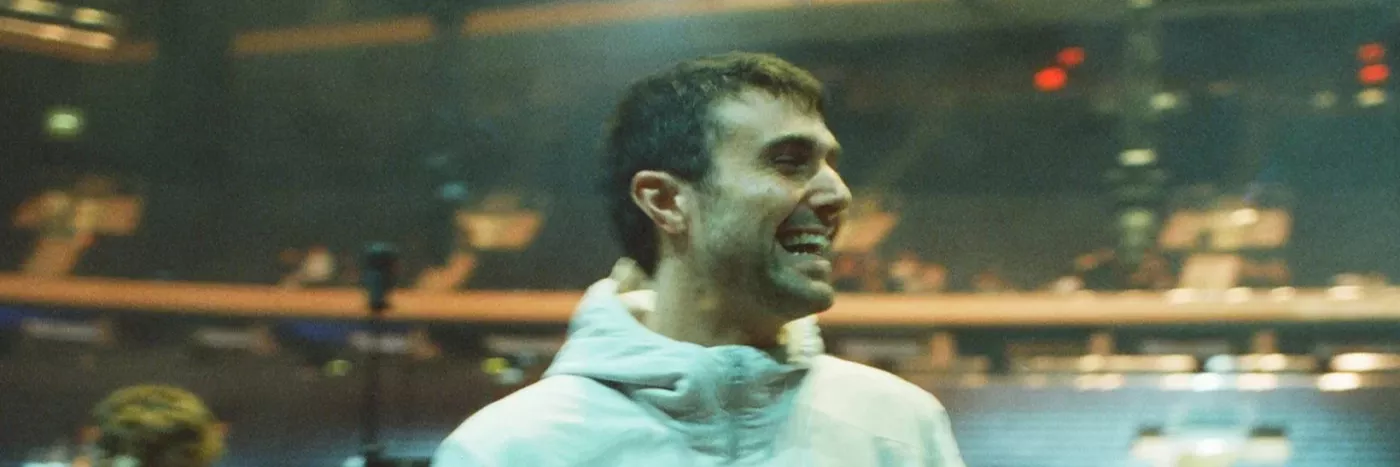 A white man in a white jacket looks over his shoulder smiling