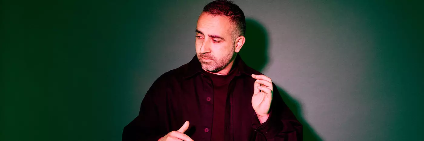 A middle aged man in a black jacket standing in dark studio lighting.