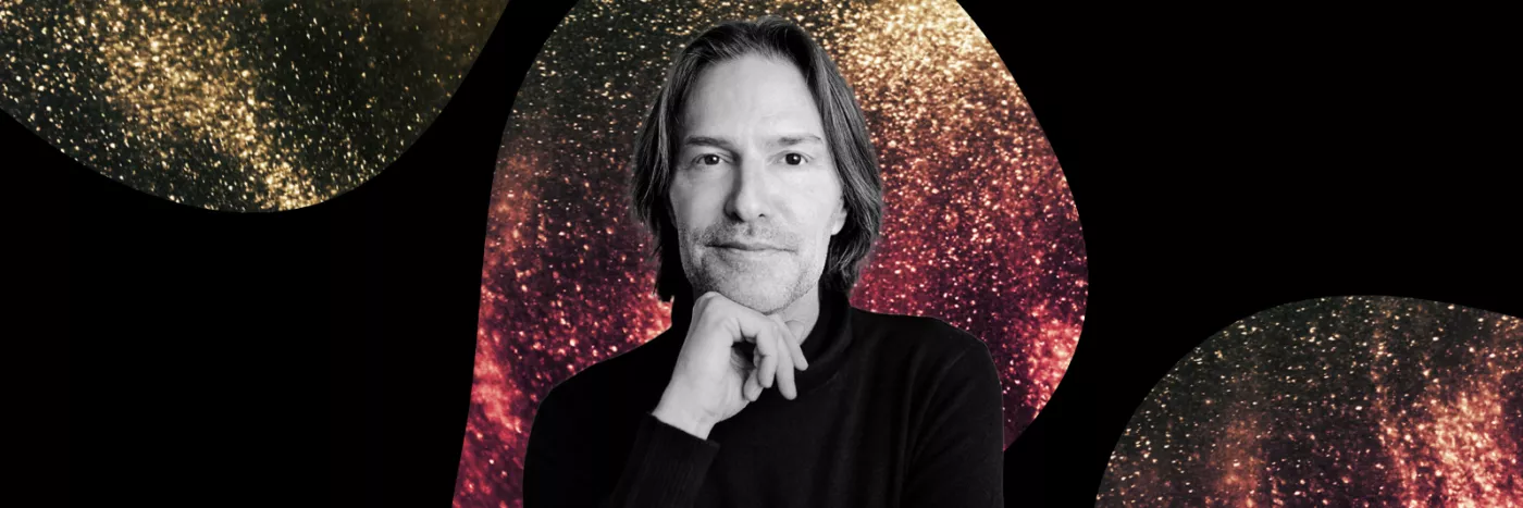A black and white photo of Conductor Eric Whiteacre with a red and yellow sparkly background