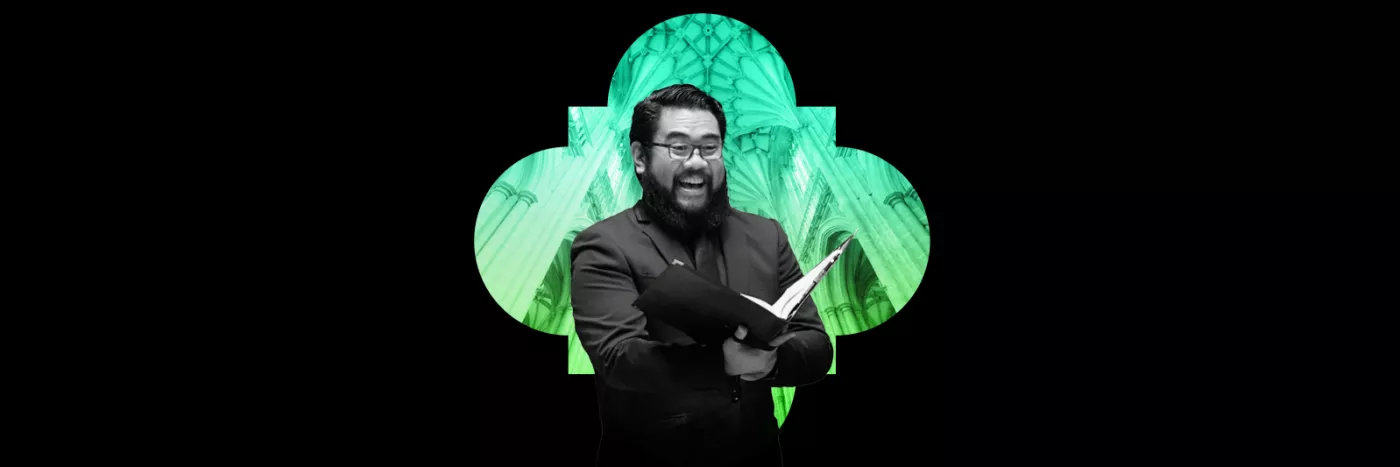 Man with a beard in a black suit sings with a cathedral as the background