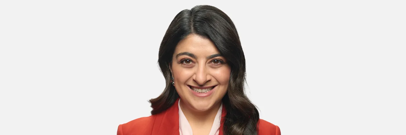 A smiling woman with dark brown hair, wearing a red blazer against a light grey background.