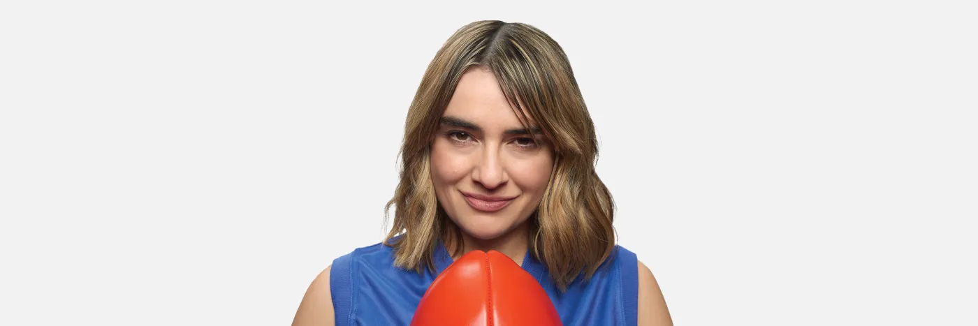 A woman with light brown shoulder length hair wearing a blue sleeveless jersey and holding a red football.