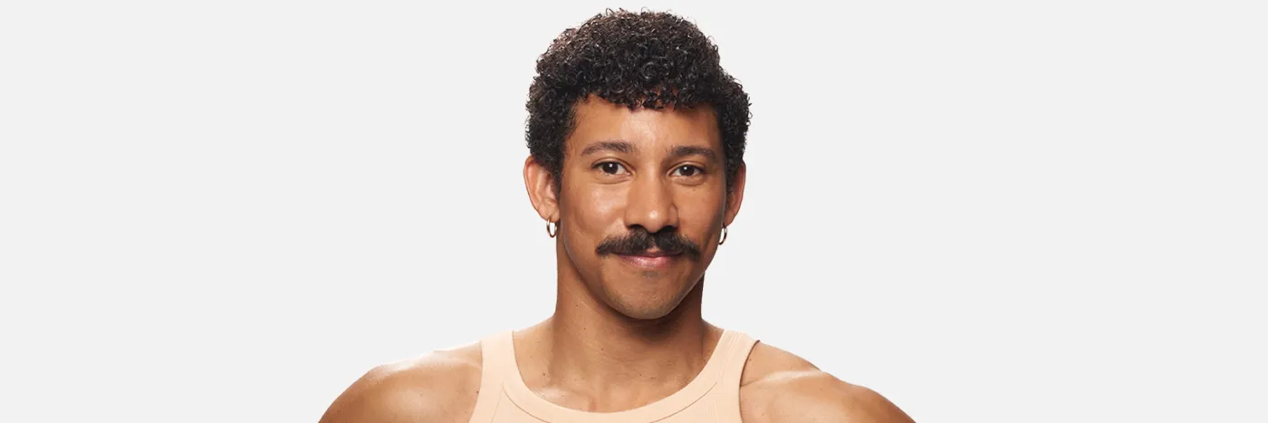 A headshot of a man with curly dark hair, wearing a peach coloured singlet against a light grey background.