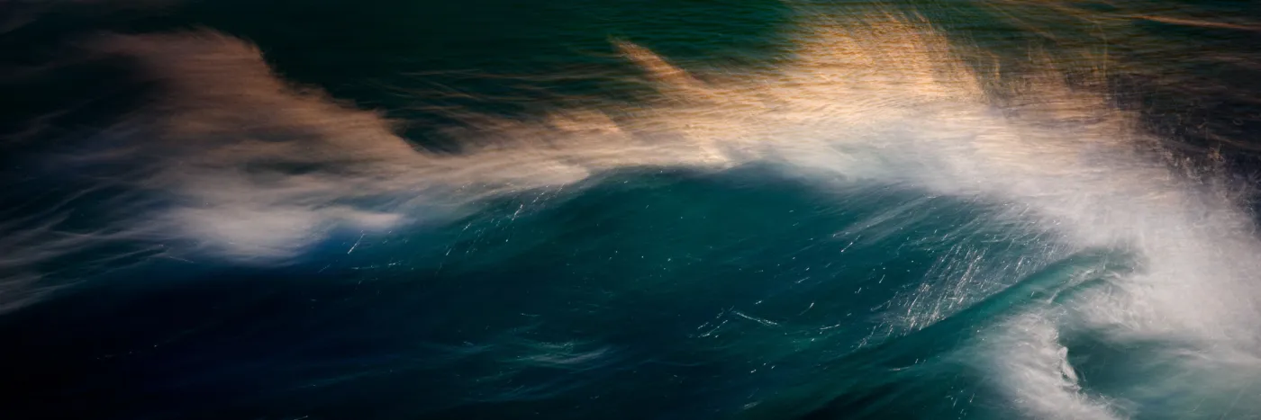 The surface of a dark body of water with light reflected of gentle waves and wind creating soft spray of whitewater.