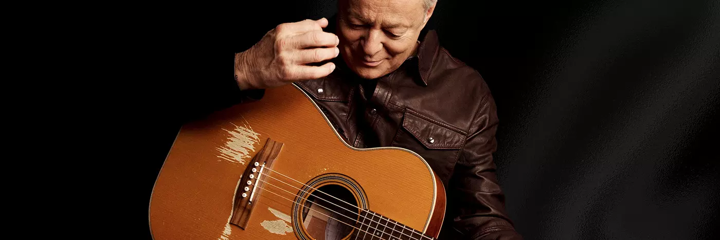 A man with grey hairs wearing a black leather jacket playing a guitar.