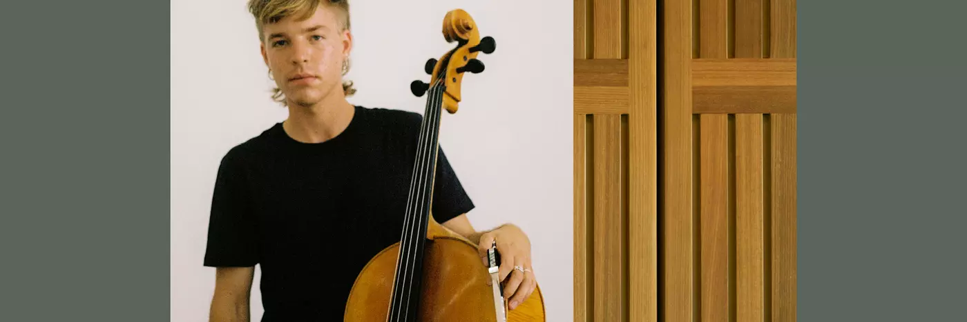 A young blonde man in black t-shirt holding a bass violin.