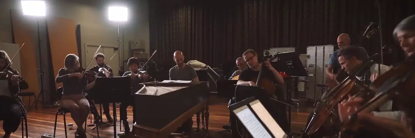 String orchestra gathered around playing in a dark lit room.