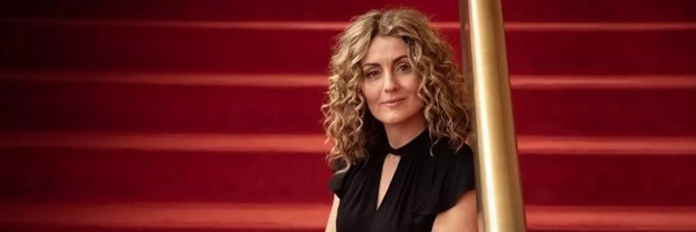 A woman with curly blonde hairs sitting on the red carpeted stairs.
