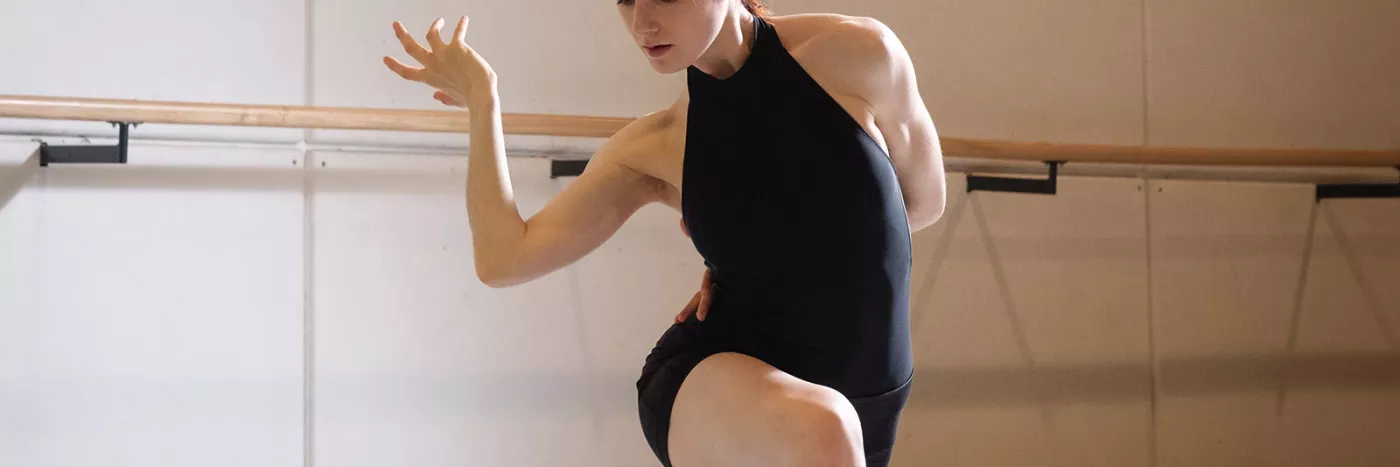 A woman in a black leotard dancing in a studio.