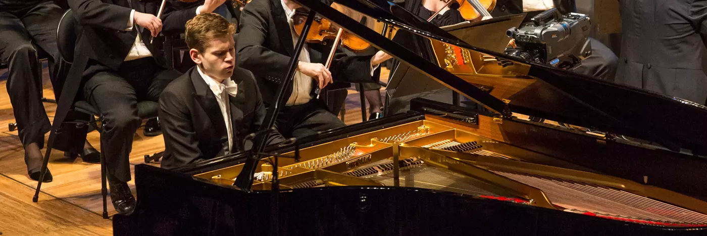 A man playing a grand piano in an orchestra.