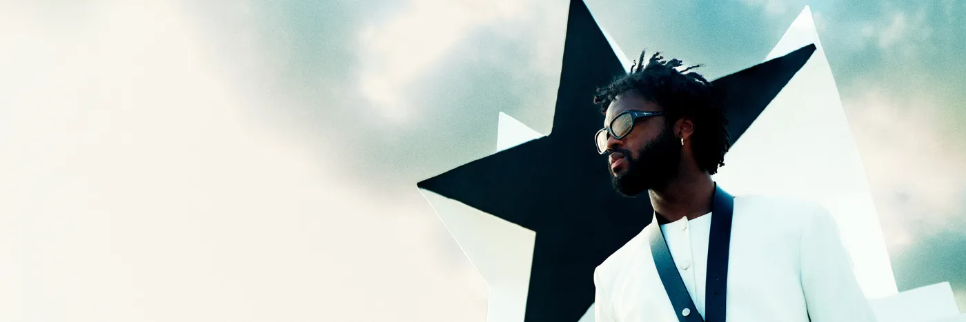 A young black man wears sunglasses and poses in front of a large black star.