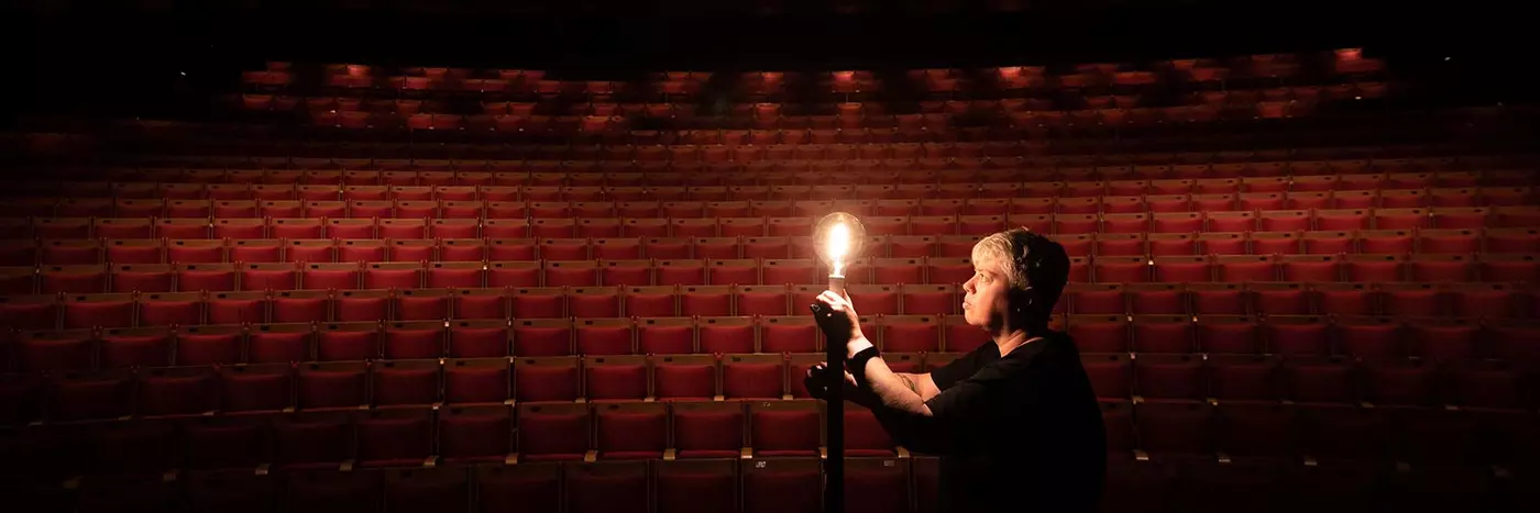 Person holding up a light in front of an empty theatre.