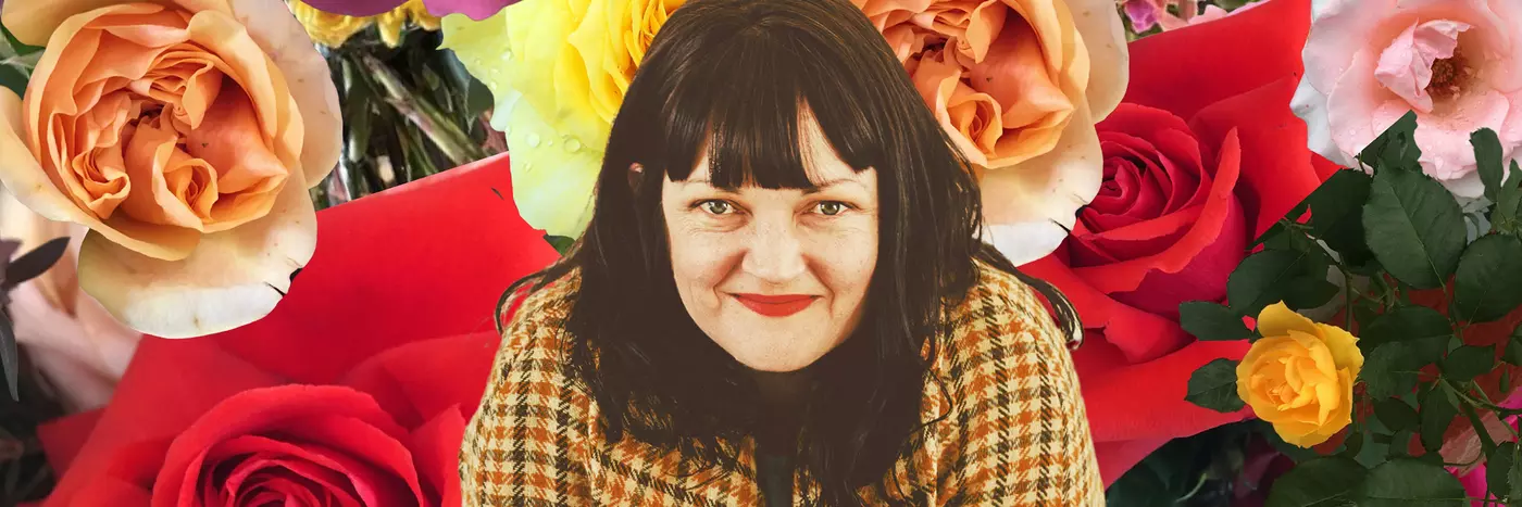 A women smiling infront of a background of flowers