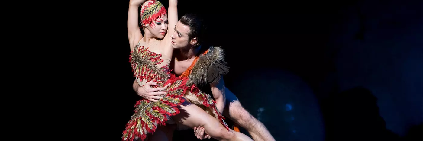 Two dancers, one in a red feathered costume.