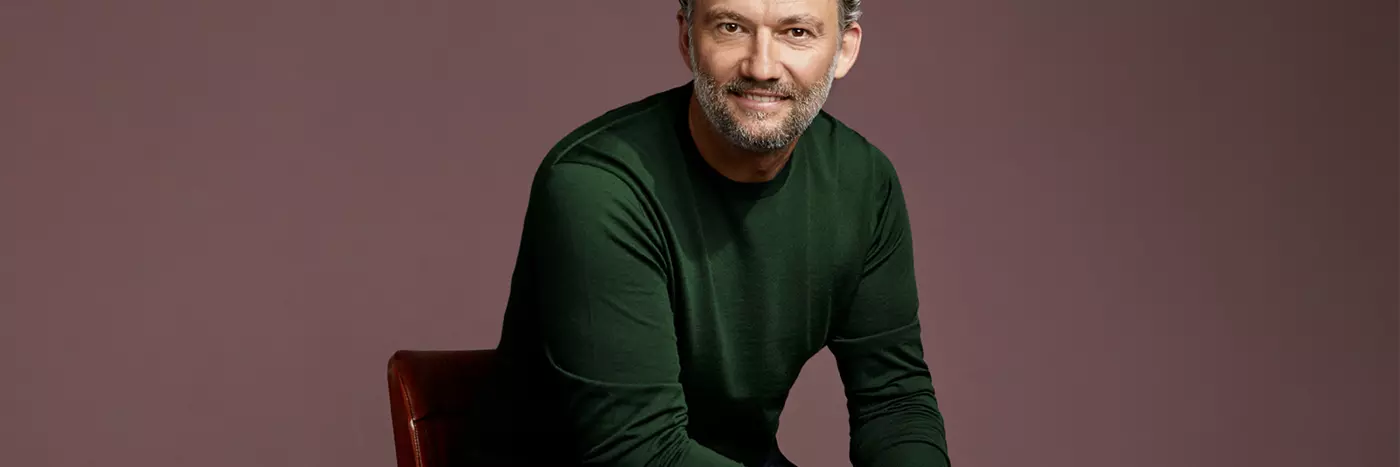 A man with grey hairs in green sweater sitting on the chair.