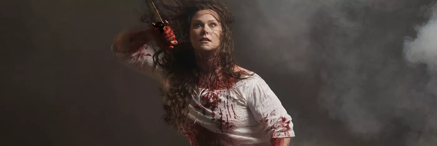 A woman holding a dagger and drenched with blood.