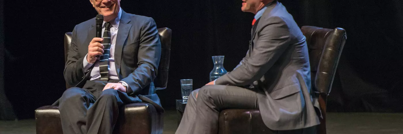 Two middle age men wearing suit, having a debate on the stage.