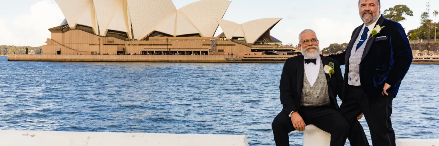 Two men stood in suits outside of the Sydney Opera House.