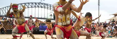 Men in sand pit performing indigenous dance in the homeground of Sydney opera house.