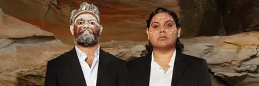 An aboriginal man and women wearing a black suit with traditional face art.