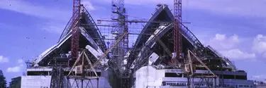 The sails of the Opera House are covered in scaffold. They sky is cloudy and blue.