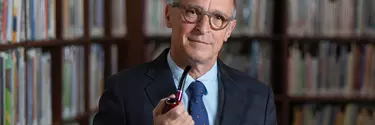David Sedaris an American humorist in a suit holding a cigar pipe.
