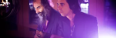 Two men in black shirts in a purple-lit studio with headphones on.
