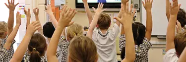 Kids in a digital classroom with their hands up in the air.