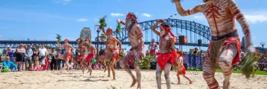 Men in sand pit performing indigenous dance in the homeground of Sydney opera house.