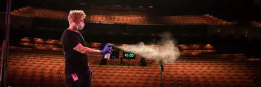 Man spraying aerosol into a microphone on stage.