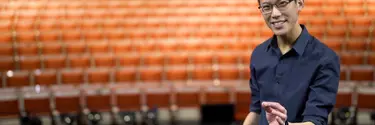 A man in a blue shirt standing in front of an empty theatre.