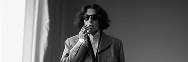 A mature white woman smoking a cigarette. The image is in black and white and she is wearing sunglasses.