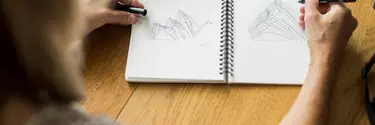 A woman drawing sketches of the Sydney Opera House in a notebook.