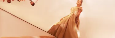 Woman in gold ballgown stands away from other partygoers
