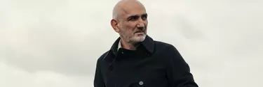 A man with grey hair in a black coat standing outside.