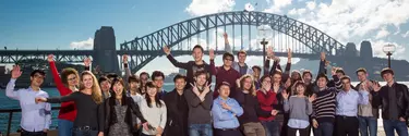 A group of people standing near Sydney opera house with Harbour bridge in the background.