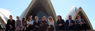 A group of men and women sitting on the staircase of Sydney opera house.