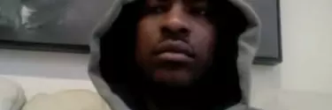 A man in a grey hoodie sat down on a couch.