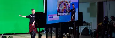 Producer's view through a screen showing a digital background, of a performer in front of a green screen