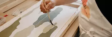 A person in an apron painting a canvas.