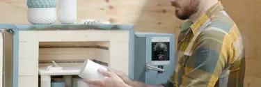 A man in a shirt crafting a white object in a wooden room.