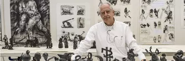 A mature man with white hair stares forward surrounded by details illustrations and sculptures.
