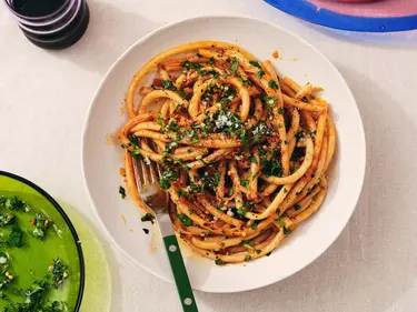 Looking down on a bowl of caramelized shallot pasta on a white tablecloth. A silver fork with a green handle is resting on the side of the bowl.