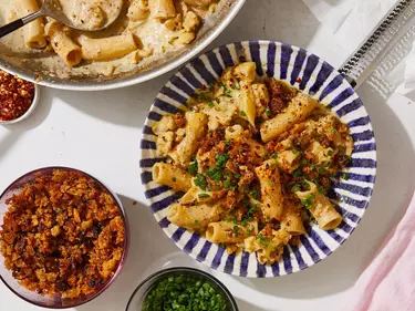 Two large bowls and three smaller bowls on a tabletop, four holding ingredients and one with the finished dish of creamy cauliflower pasta with pecorino bread crumb.